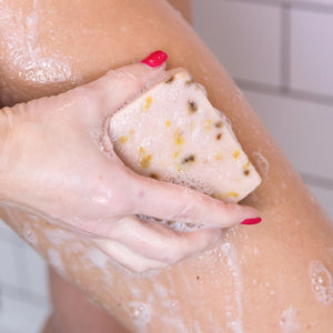 Hand scrubbing a person's leg with a soap bar in a bathroom setting
